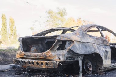 Şehirdeki yolda park etmiş hızlı bir araba yanmış. Araba artığı.
