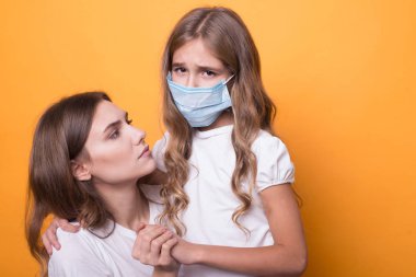 Anne, turuncu arka planda tıbbi maskeli kızına iyi bak. hastalıktan kurtulma