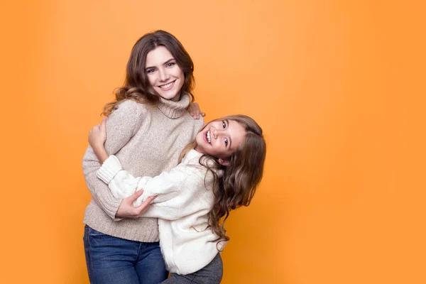Mutlu bir aile. Süveter giymiş, turuncu arka planda sarılan güzel bir kızı olan bir anne.
