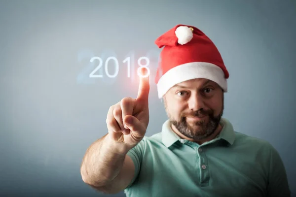 Glücklicher bärtiger Mann mittleren Alters mit Weihnachtsmütze drückt den Knopf Stockbild