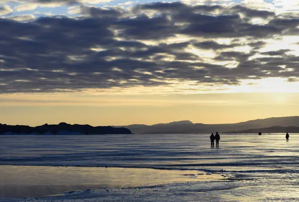 Kışın gün doğumu Baykal. Güneş bulutları delip geçer ve buzun yüzeyini yansıtır.