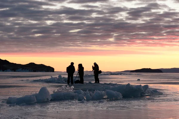 Güneş doğarken Baykal Gölü 'nün buzundaki insanlar.