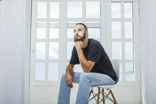 Young man in jeans with a beard a hipster sitting on a chair on