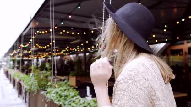 Jonge vrouw met hoed wandelen in de buurt van koffiehuis versierd met holiday lights — Stockvideo