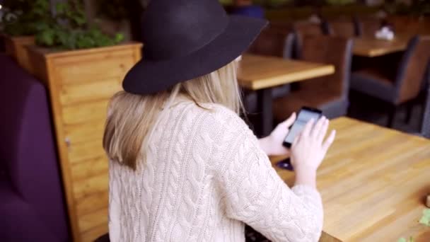 Młoda kobieta, pisania wiadomości na telefon przy stoliku w kawiarni — Wideo stockowe