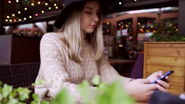 Mladá žena psaní zprávy v telefonu, posezení v kavárně vyzdoben vánočními světly — Stock video