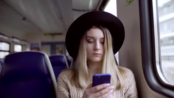 Young woman typing message on her phone and smiling, sitting in electric train — Stock Video