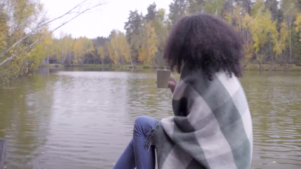 Cute black girl wrapping herself in woolen plaid and drinking hot tea — Stock Video