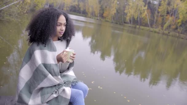 Linda chica negra envolviéndose en cuadros de lana y bebiendo té caliente — Vídeo de stock