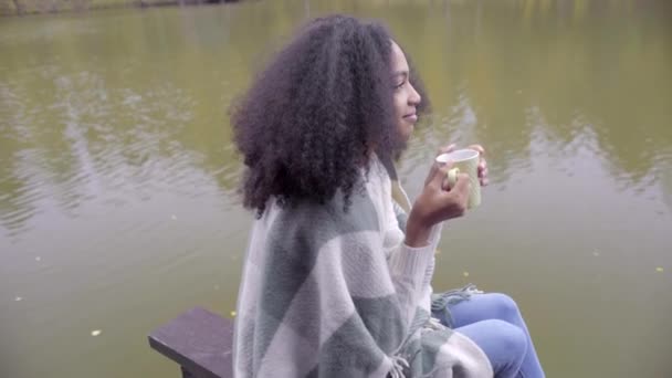 Cute black girl wrapping herself in woolen plaid and drinking hot tea — Stock Video