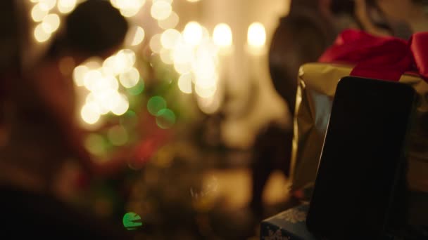 Kapcsolat nélküli telefon ajándék doboz, és a középpontjában nő díszíti a karácsonyfát a háttérben — Stock videók
