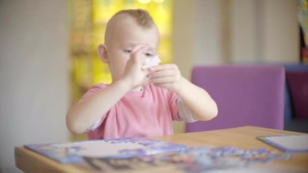 Маленький мальчик собирает головоломки на столе — стоковое видео