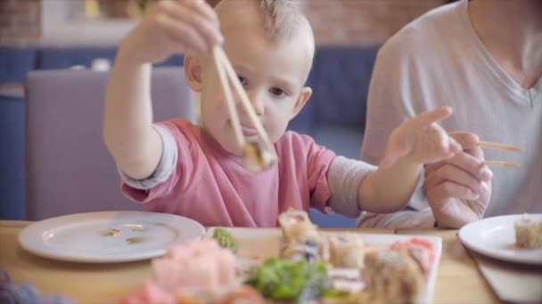 Little boy eating Japanese sushi and rolls with sticks by himself — Stock Video