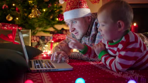 Jongetje kijken cartoons op laptop met zijn vader op kerstavond — Stockvideo