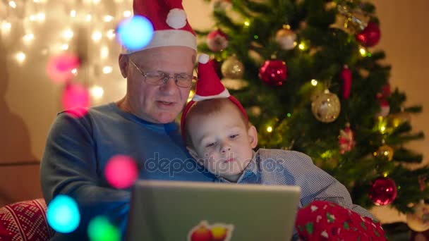 Neto e avô assistindo desenhos animados perto da árvore de Natal — Vídeo de Stock