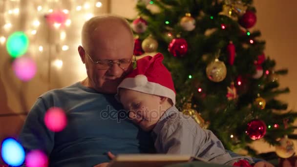 Μικρό αγόρι υλοτόμηση κοιμάται κατά τη διάρκεια του gradpa ανάγνωση βιβλίων σε αυτόν την παραμονή των Χριστουγέννων — Αρχείο Βίντεο