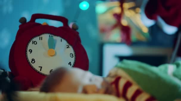 Ritratto ravvicinato di un bel bambino che dorme nella sua branda la notte di Natale. L'orologio giocattolo colpisce a mezzanotte. Il regalo di Natale è sullo sfondo — Video Stock