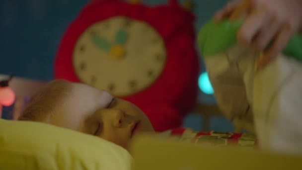 Il bambino dorme nella culla la notte di Natale. Mamma lo sta coprendo con coperta e baci sulla guancia — Video Stock