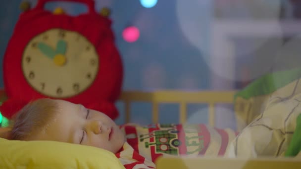 Le petit garçon dort dans son lit le soir de Noël. Papa le couvre de couvertures et l'embrasse sur la joue. — Video