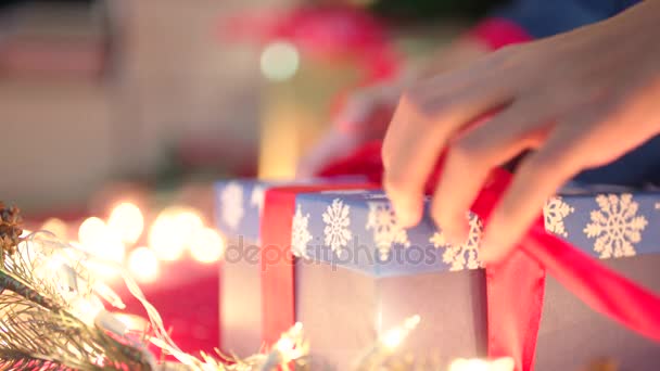 Kerst geschenkverpakking. Handen binden een cadeau met een rood lint op kerstavond — Stockvideo