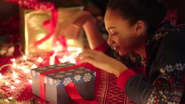 Νεαρή μαύρη γυναίκα είναι openning ένα κουτί δώρου με κόκκινη κορδέλα βραδιά των Χριστουγέννων — Αρχείο Βίντεο