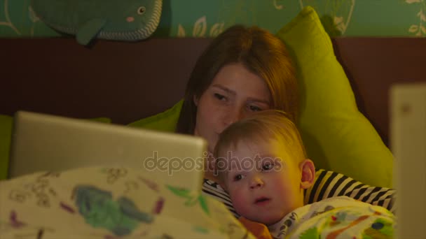 Mom and her son watching cartoons for night in the bed — Stock Video