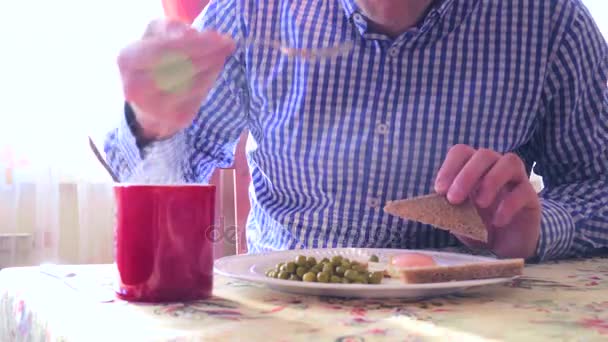 Man met ontbijt van gebakken eieren met doperwtjes en toast, warme koffie met stoom in tegenlicht — Stockvideo