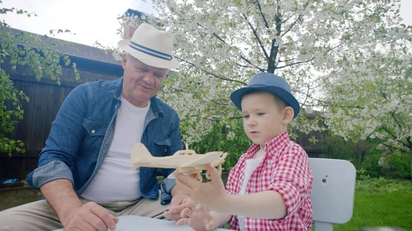 祖父と孫は、裏庭で、夏に、木製の飛行機を作っています。 — ストック写真