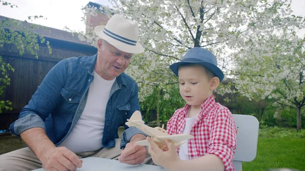 Opa und Enkel basteln im Sommer im Hinterhof ein Holzflugzeug — Stockfoto