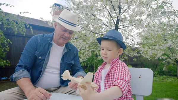 Opa und Enkel basteln im Sommer im Hinterhof ein Holzflugzeug — Stockfoto