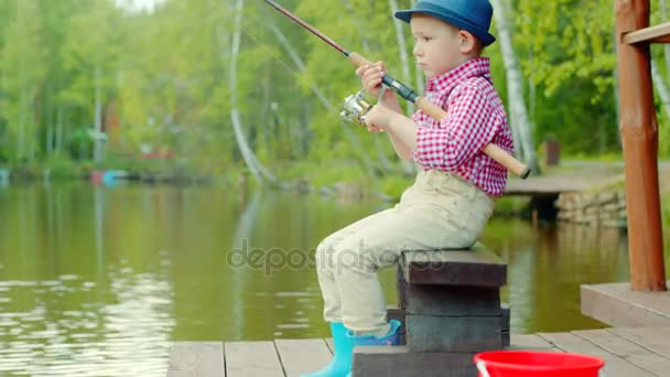 Little boy in straw hat with spinning on freshwater fishing at the lake — Stock Footage Little boy in straw hat with spinning on freshwater fishing at the lake Video Clip
