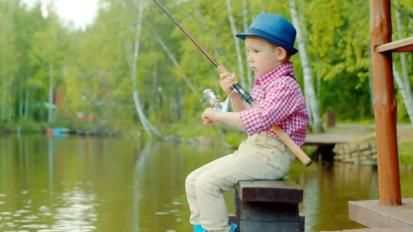 Mały chłopiec w słomkowy kapelusz z przędzenia na połowy ryb słodkowodnych, nad jeziorem — Zdjęcie stockowe