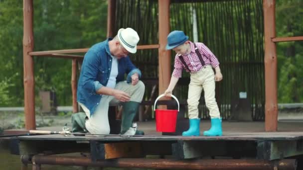 Pequeño niño está ayudando a su abuelo a eliminar el salmón capturado del gancho y poner en el cubo de pesca en el lago — Vídeo de stock