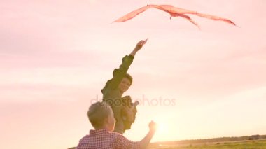 Küçük çocuk ve annesi uçan uçurtma günbatımında oynuyorlar