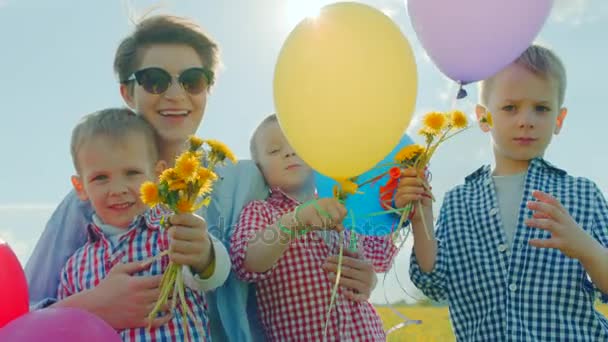 Tres niños pequeños y su mamá sonriendo con globos de color y flores — Vídeo de stock