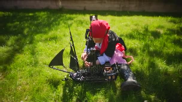 Little boy wearing pirate costume is playing in toy ship of pirates of caribbean on the lawn on Halloween — Stock Video