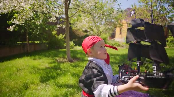Liten pojke bär pirate kostym spelar i leksak piratskepp på gräsmattan — Stockvideo