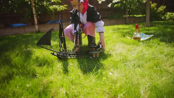 Korsan kostüm giyen küçük çocuk oyuncak gemi Karayip Korsanları'nın bahçesinde, Cadılar Bayramı'nda oynuyor — Stok video
