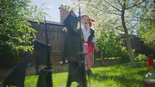 Liten pojke bär pirate kostym spelar i leksak shipen av pirater i Västindien på gräsmattan på Halloween — Stockvideo