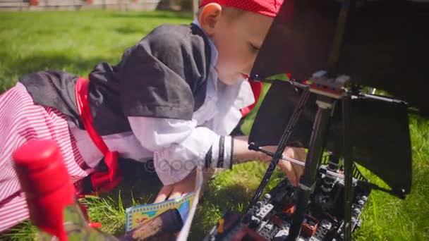 ハロウィーンの芝生の上のカリブの海賊のおもちゃの船で海賊の衣装を着て少年を再生します。 — ストック動画