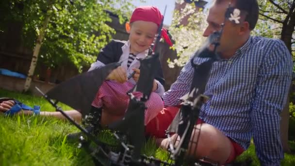 Kleiner Junge im Piratenkostüm und sein Vater erkunden Piratenschiff auf dem Rasen — Stockvideo