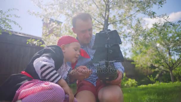 Little boy in pirate costume and his father are playing in pirate ship on the lawn — Stock Video