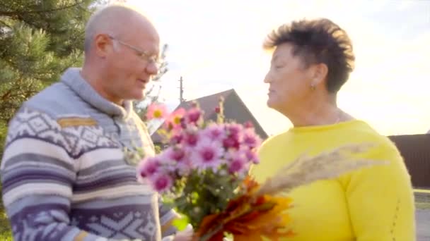 Yaşlı adam karısı için çiçek veriyor ve gün batımında öpüşüyorlar — Stok video