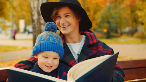 Malý chlapec a jeho matka jsou čtení knihy v podzimní park — Stock fotografie