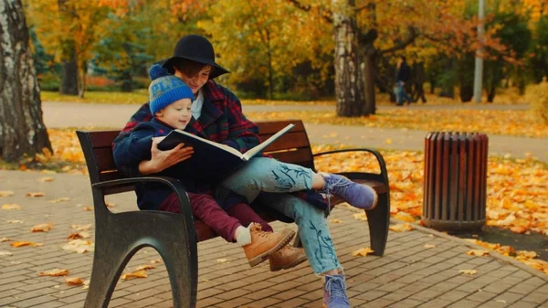 Pequeño niño y su madre están viendo álbum familiar en el parque de otoño —  Fotos de Stock