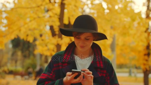 Mujer joven está llamando a alguien por teléfono mientras camina en el parque de otoño — Vídeo de stock