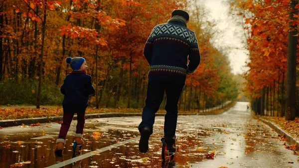 लहान मुलगा आणि त्याचे आजोबा शरद ऋतूच्या उद्यानात किक स्कूटर स्वार आहेत — स्टॉक फोटो, इमेज