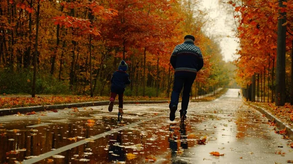 Niño y su abuelo están montando patinetas juntos en el parque de otoño — Foto de Stock