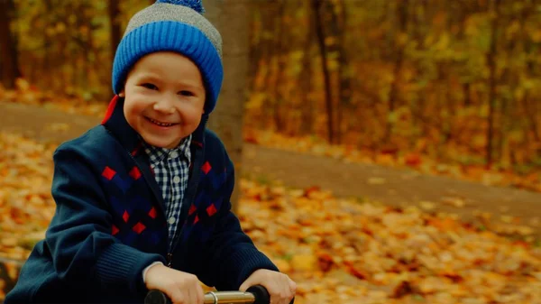 Niño pequeño está montando patinete scooter en el parque de otoño — Foto de Stock