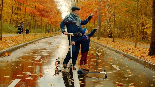 Kisfiú és a nagyapja kick robogók együtt az őszi park lovaglás — Stock Fotó